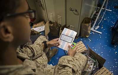 A U.S. Marine opens a care package aboard the amphibious dock landing ship USS Comstock. Photo by Lance Cpl. Gadiel Zaragoza/Provided by DVIDS (The appearance of U.S. Department of Defense (DoD) visual information does not imply or constitute DoD endorsement.)